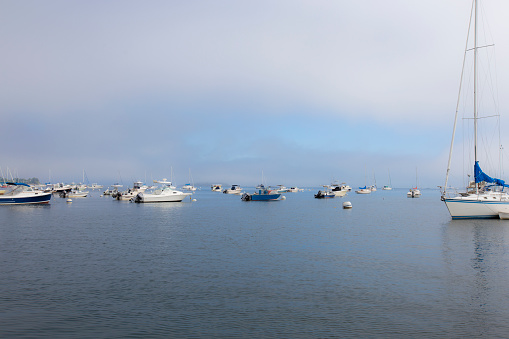 Fog lifting around a number of anchored boats in a harbor in Falmouth, Maine, USA