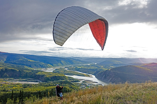 Young millennial male preparing para-glide for start from hill in Alaska close to Dawson City.