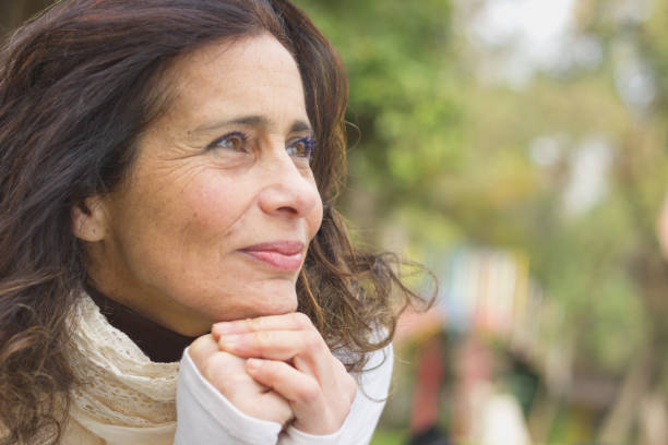 la gentille dame d’âge moyen avec regard optimiste au repos de visage sur ses mains dans le parc - différence dâge photos et images de collection