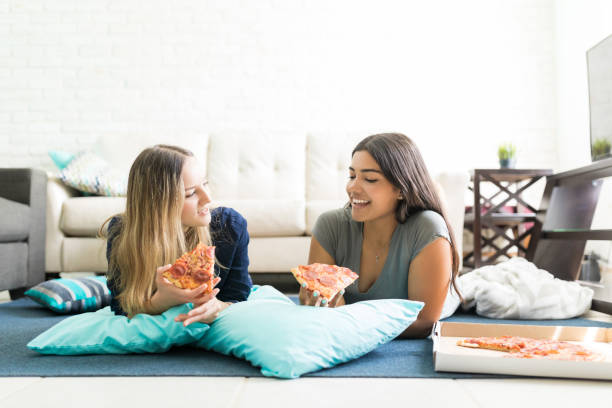 Young women holding pizza slices while lying on floor during party at home