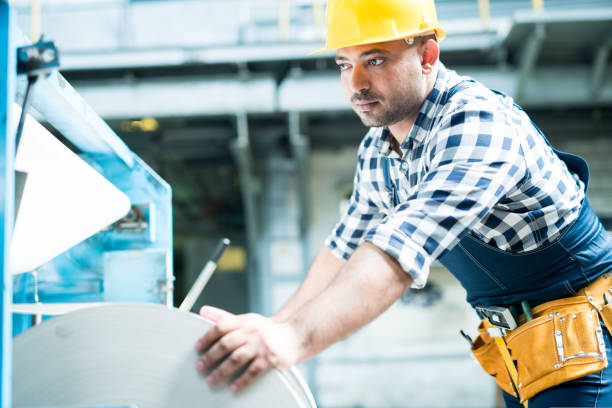 istock Serious handsome worker with tool belt controlling machinery production while leaning on machine at factory 1043882166