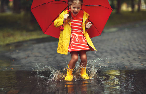 happy child girl with an umbrella and rubber boots in puddle  on autumn walk - rainbow umbrella descriptive color multi colored imagens e fotografias de stock