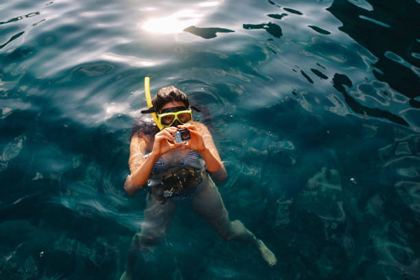 Young woman snorkeling near Phi Phi islands, in Thailand. She is setting up her small action camera, getting ready to dive and enjoy the beautiful underwater view.