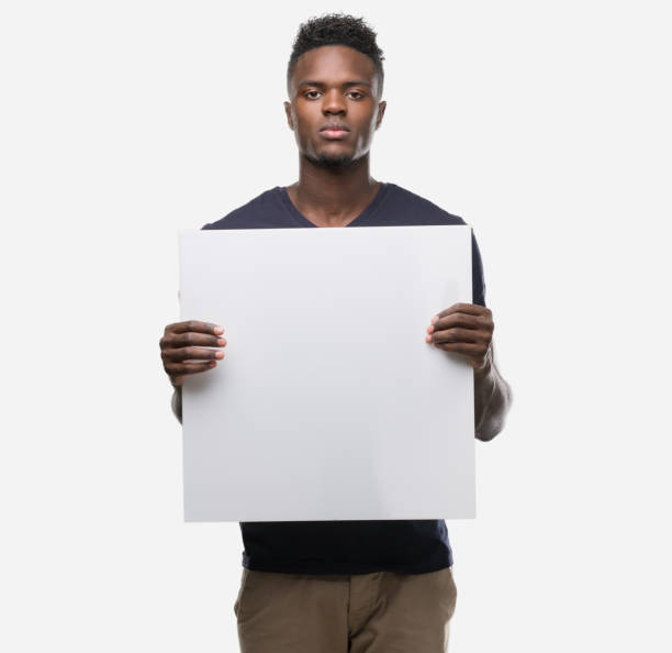 młody afroamerykanin trzyma transparent z pewnym wyrazem inteligentnego myślenia o twarzy poważnie - man holding a sign zdjęcia i obrazy z banku zdjęć