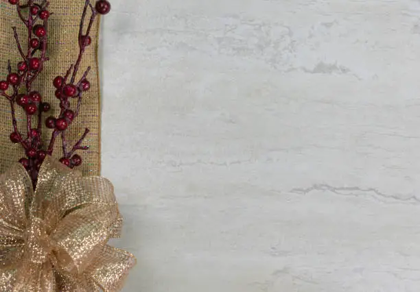 A gold bow and red berries on a burlap ribbon along the left side with copy space