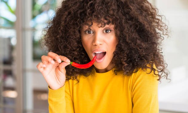 african american woman eating red hot chili pepper scared in shock with a surprise face, afraid and excited with fear expression - vegetable pepper food chili pepper imagens e fotografias de stock