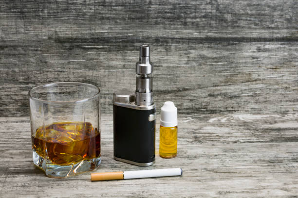 istock Whiskey in a glass with an e-cigarette and liquid for it on a gray stone background 1043969448