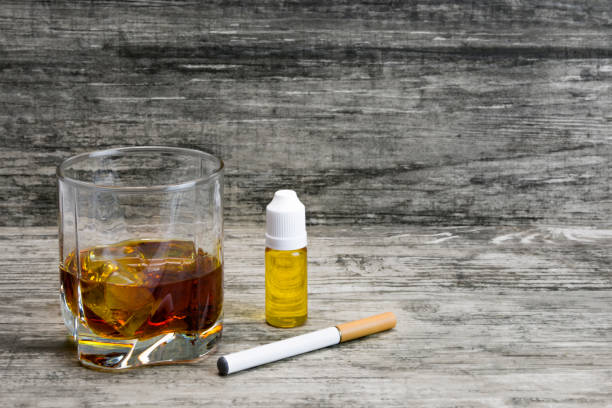 istock Whiskey in a glass with an e-cigarette and liquid for it on a gray stone background 1043969462