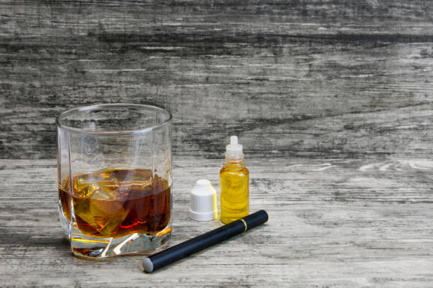 istock Whiskey in a glass with an e-cigarette and liquid for it on a gray stone background 1043969484