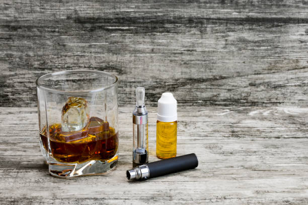 istock Whiskey in a glass with an e-cigarette and liquid for it on a gray stone background 1043971436