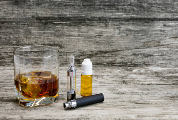 istock Whiskey in a glass with an e-cigarette and liquid for it on a gray stone background 1043971666