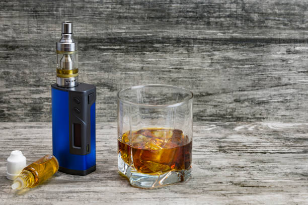 istock Whiskey in a glass with an e-cigarette and liquid for it on a gray stone background 1043971686