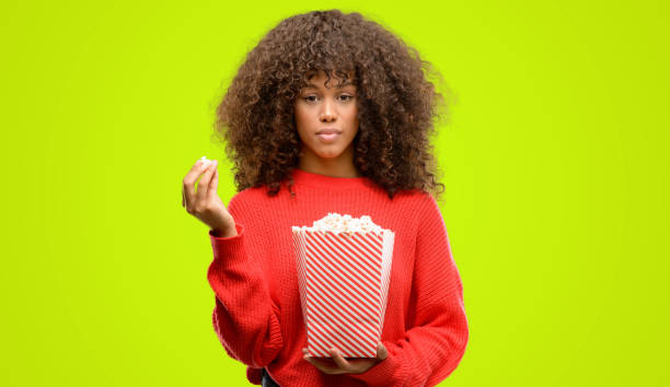 istock African american woman eating popcorn with a confident expression on smart face thinking serious 1043972944