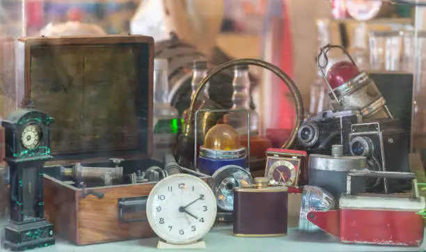 Photo of Assorted vintage items, clocks, cameras, flasks, sextant, lamps behind shop window.