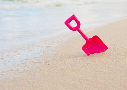 Closeup of a plastic pink kid's shovel next to the beach shoreline.