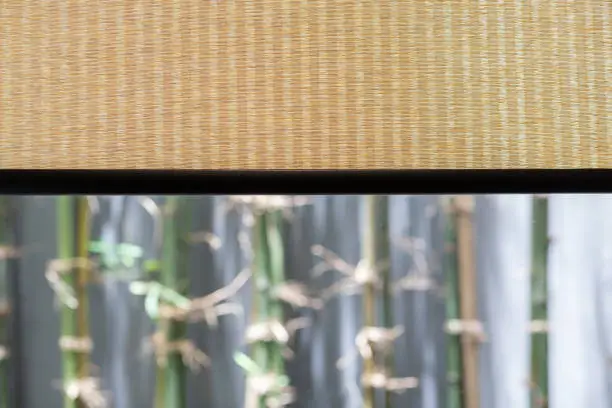 Photo of Bamboo curtain weave texture with outdoor tree background.