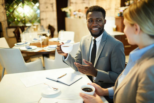 istock Cheerful handsome young black businessman with beard drinking coffee and gesturing hand while sharing plans with business partner 1044046494