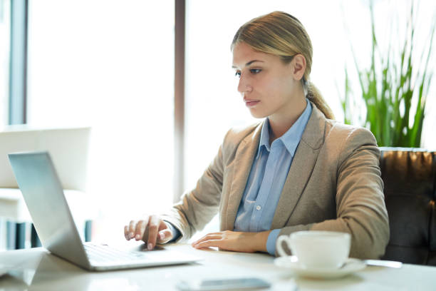 istock Serious concentrated female manager in jacket sitting at table and using laptop while working in coffee shop 1044046722