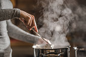 Unrecognizable woman making lunch in the kitchen and stirring soup.