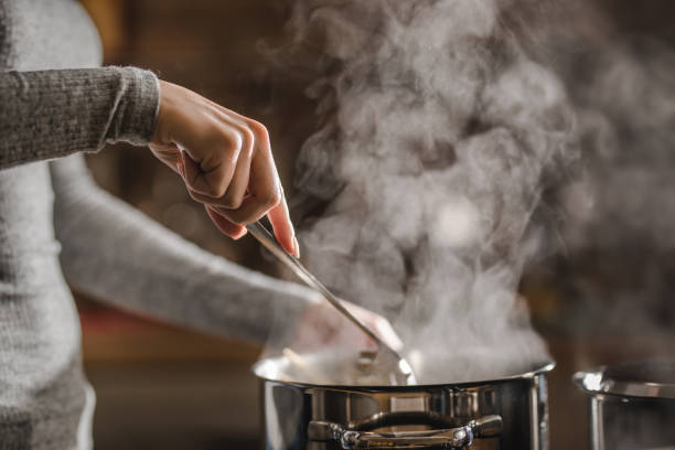 Unrecognizable woman making lunch in the kitchen and stirring soup. Unrecognizable woman stirring soup in a saucepan while making lunch. soup photos stock pictures, royalty-free photos & images