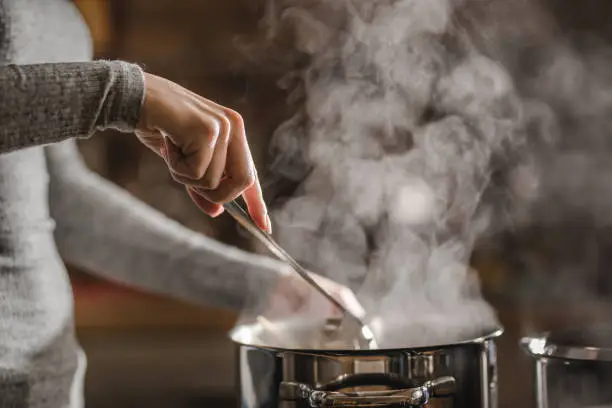 Unrecognizable woman stirring soup in a saucepan while making lunch.