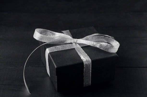 Black gift box with silver ribbon bow on black background.