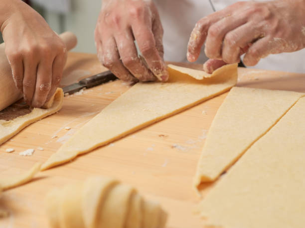 istock Chef hands are rolling a croissant from dough on wooden board. black background. 1044083560