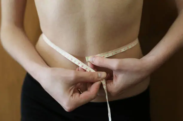 Slim girl is measuring her waist with a centimetre tape measure at home. Fit sport healthy photo. Successful diet.