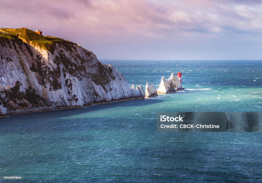 A break in the clouds illuminates the iconic chalk stone pinnacles of The Needles and the 19th century lighthouse on the coastline Isle of Wight an island off the south coast of England Isle Of Wight Stock Photo