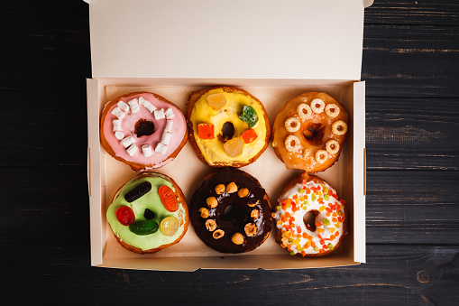 Six colorful round donuts with sprinkles in the box. Flat lay, top view.