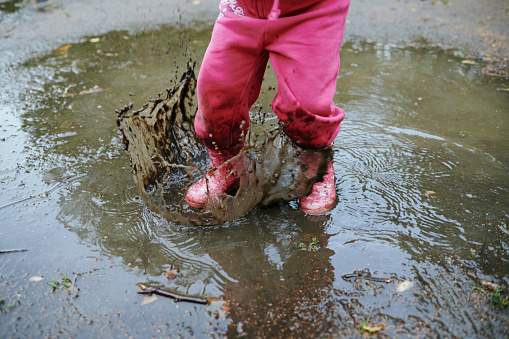 Child jumps in a dirty puddle in pink rubber boots