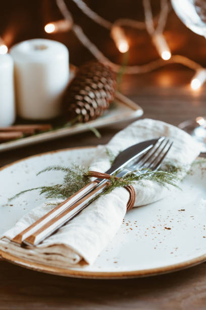 istock Thanksgiving table setting among white candles and cones. Ceramic plate with fork and knife on a linen napkin. The concept of a festive dinner. 1044136052