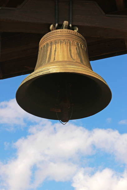 old metal church bell hanging in front of blue and white sky
