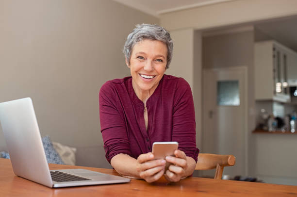 happy mature woman using smartphone - senior adult happiness computer looking at camera imagens e fotografias de stock