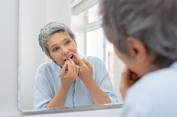 Mature woman cleaning teeth with floss Mature beautiful woman cleaning her teeth with floss in bathroom. Reflection of senior woman in bathroom mirror while cleaning teeth with dental floss. Healthcare and oral hygiene concept. vanity mirror photos stock pictures, royalty-free photos & images