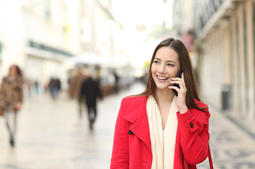 Front view portrait of a happy woman talking on phone walking in the street in winter