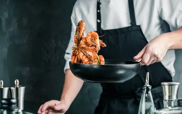 Photo of Chef cooking with Tiger prawn on dark background