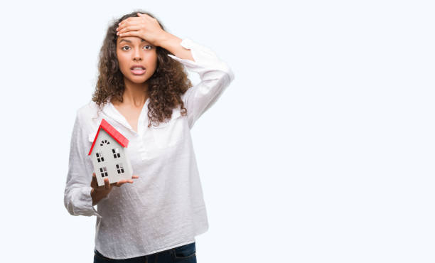 Young hispanic real state agent woman holding small house stressed with hand on head, shocked with shame and surprise face, angry and frustrated. Fear and upset for mistake. Young hispanic real state agent woman holding small house stressed with hand on head, shocked with shame and surprise face, angry and frustrated. Fear and upset for mistake. frustrated homebuyer stock pictures, royalty-free photos & images