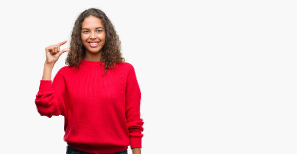 istock Young hispanic woman wearing red sweater smiling and confident gesturing with hand doing size sign with fingers while looking and the camera. Measure concept. 1044207780