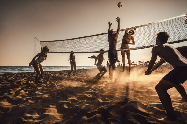 large group of friends playing beach volleyball at sunset. - volleyball beach volleyball beach sport imagens e fotografias de stock