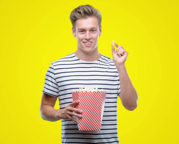 istock Young handsome blond man eating popcorn with a happy face standing and smiling with a confident smile showing teeth 1044213564