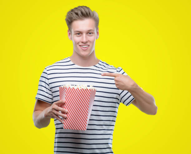 istock Young handsome blond man eating popcorn with surprise face pointing finger to himself 1044213578