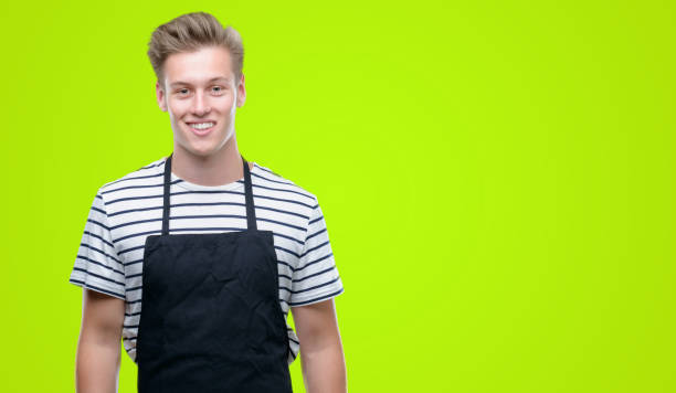 istock Young handsome blond man wearing apron with a happy face standing and smiling with a confident smile showing teeth 1044214596