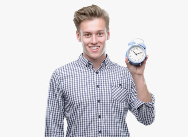 istock Young handsome blond man holding alarm clock with a happy face standing and smiling with a confident smile showing teeth 1044216310