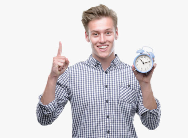 istock Young handsome blond man holding alarm clock surprised with an idea or question pointing finger with happy face, number one 1044216350