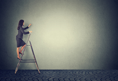 Side view of formal businesswoman climbing ladder against gray wall having career promotion
