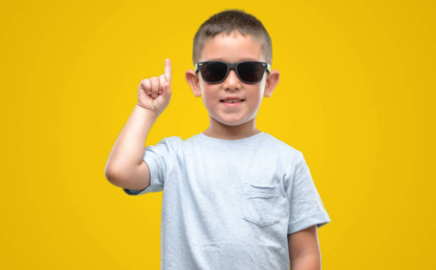 istock Dark haired little child wearing sunglasses surprised with an idea or question pointing finger with happy face, number one 1044220516