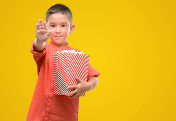 istock Dark haired little child eating popcorn with open hand doing stop sign with serious and confident expression, defense gesture 1044222924