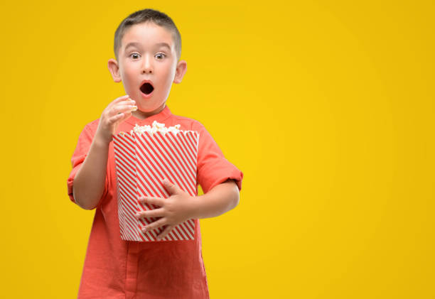 Dark haired little child eating popcorn scared in shock with a surprise face, afraid and excited with fear expression
