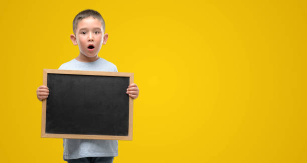 istock Dark haired little child holding a blackboard scared in shock with a surprise face, afraid and excited with fear expression 1044223324